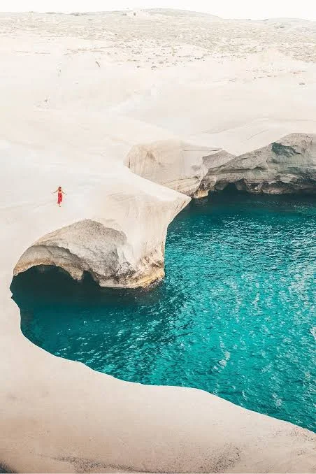 Person standing on white rock formations above a turquoise cove